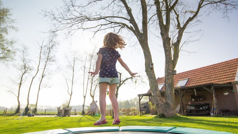 Dziewczynka skacząca na trampolinie w ogrodzie przed swoim domem